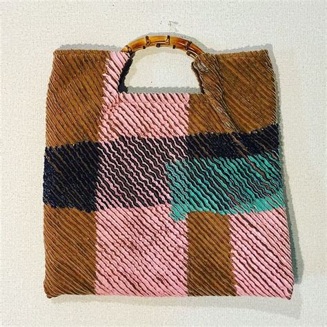 A Pink Brown And Blue Bag With Bamboo Handles On A White Surface Next