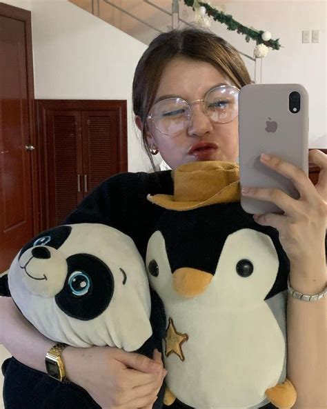 A Woman Holding A Cell Phone While Wearing A Stuffed Penguin And Panda