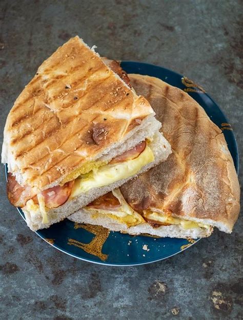 A Sandwich Cut In Half Sitting On Top Of A Blue Plate With Cheese And Bacon