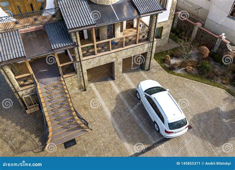 New White Car Parked In Paved Driveway With Green Lawn Decorative Bushes And Brick Fence Of Big