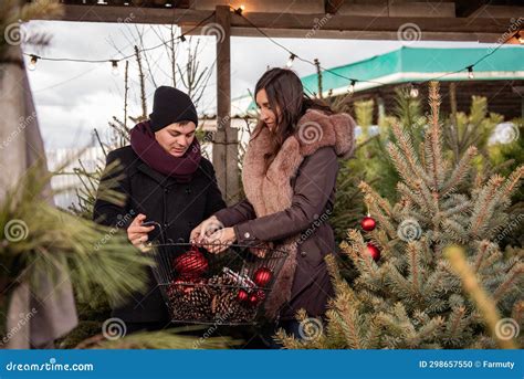 Funny Couple Decorates Christmas Trees At Market With Red Balls Man And Woman Hang Toys On Fir