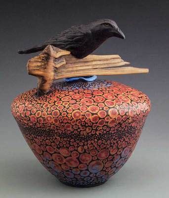 A Black Bird Sitting On Top Of A Red And Blue Vase With Wooden Sticks