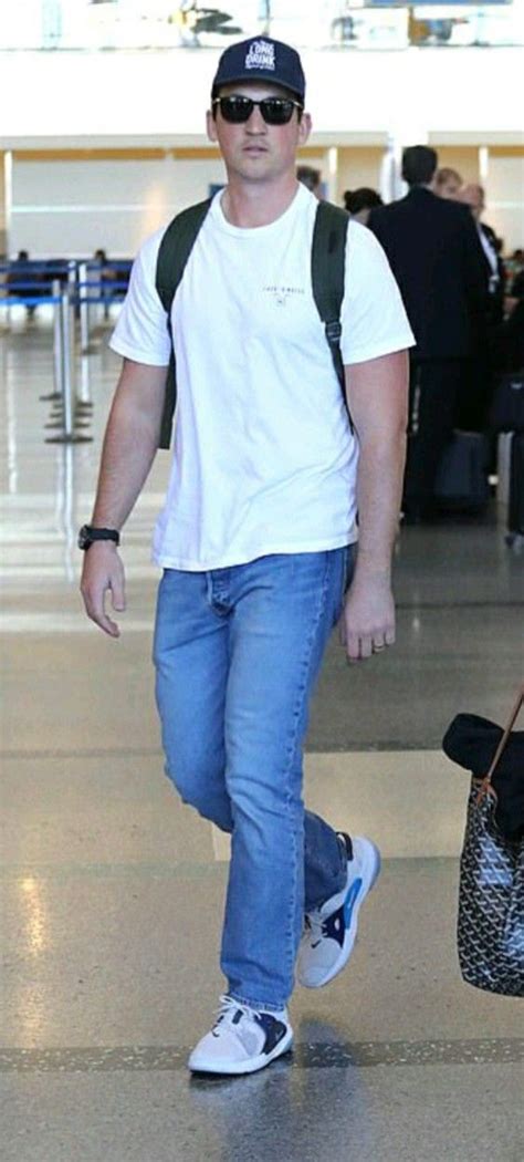 A Man Walking Through An Airport Carrying A Bag And A Handbag On His