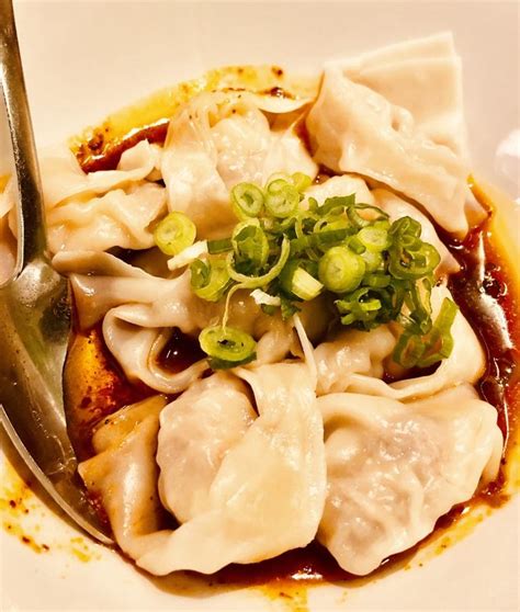 a white plate topped with dumplings covered in sauce and scallions next to a fork