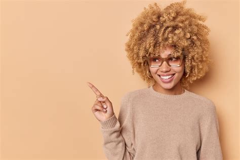 Una mujer joven y positiva de cabello rizado sonríe alegremente y