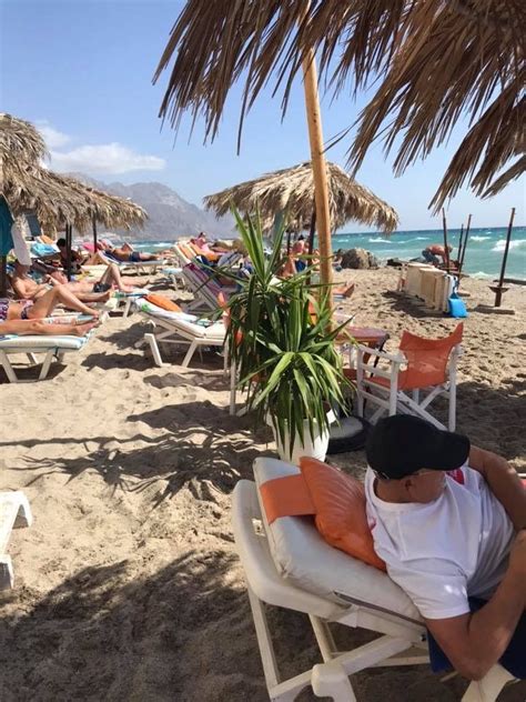 A Man Laying On Top Of A White Beach Chair Under A Palm Tree Next To