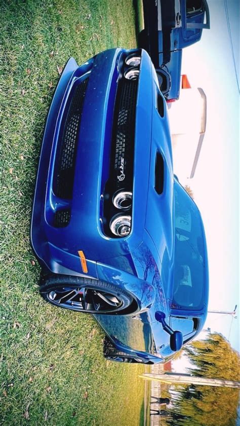 The Front End Of A Blue Sports Car Parked On Top Of A Grass Covered Field