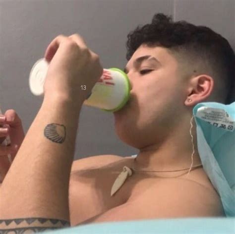 A Man Laying In Bed Drinking Out Of A Cup With Ear Buds On His Ears