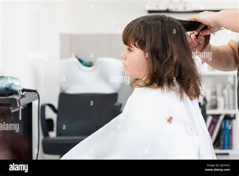 Hands of crop anonymous hairdresser cutting dark hair of cute girl ...