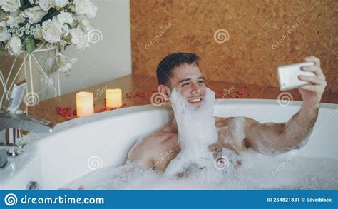 Cheerful Man With Foam On Beard Is Taking Selfie Using Smartphone In Hot Tub In Modern Spa Salon