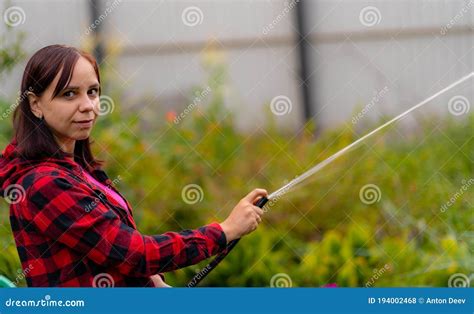 Rear View Of Young Woman Watering Vegetable Garden From Hose Close Up