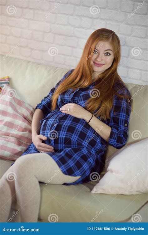 Red Haired Young Pregnant Woman Sitting At Home On The Couch And Stock