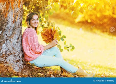 Happy Smiling Woman With Yellow Maple Leafs Sitting Under Tree In Sunny