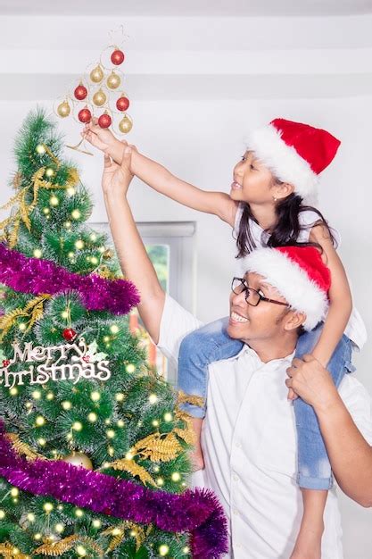 Premium Photo Cheerful Daughter Decorating Christmas Tree While Sitting On Fathers Shoulders