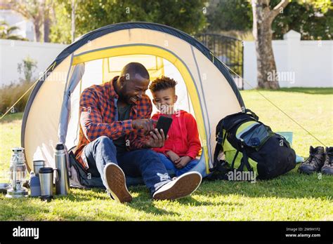 Happy African American Father And Son Sitting In Tent And Using