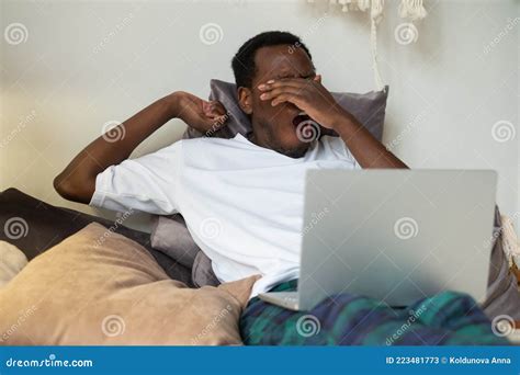 African Man Working Lying On Bed At Home Being Tired Yawning Stock