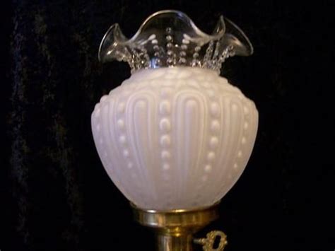 A White Glass Lamp With Gold Trimmings On The Base And A Black Background