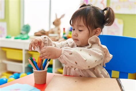 Adorable Chinese Girl Preschool Student Sitting On Table Holding Pencil