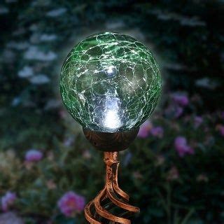 A Green Glass Ball Sitting On Top Of A Metal Stand In Front Of Some Flowers