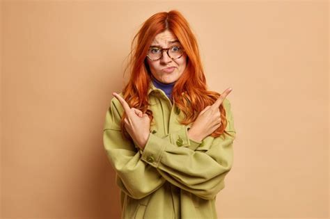 Free Photo Hesitant Redhead Young Woman Points Sideways As Tries To