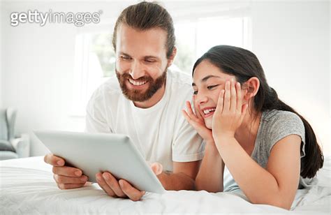 Happy Caucasian Father And Daughter Holding Digital Tablet While Lying Together On A Bed