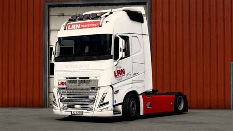 A Large White Truck Parked In Front Of A Red Building With An Open Door