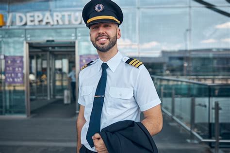 Premium Photo | Cheerful young man airline captain in pilot hat looking at camera and smiling