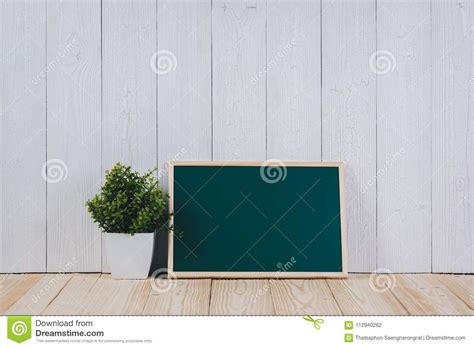 Blank Green Chalkborad With Wood Frame And Little Decorative Tree In White Vase On Wooden Table