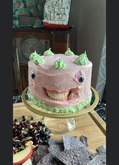 A Pink Cake With Green Icing And Smiling Face On A Gold Platter Next To