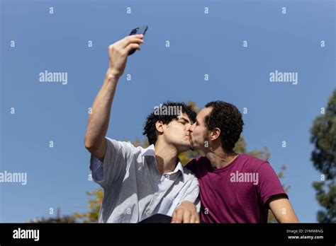 Happy Gay Couple Kissing While Taking A Selfie With A Smartphone Outdoors Copy Space Stock