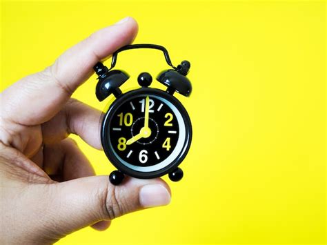 Premium Photo Hand Holding Vintage Black Alarm Clock On Yellow Background