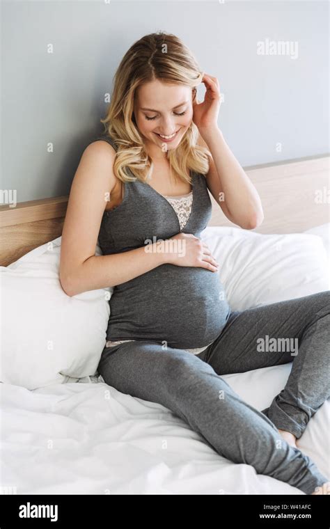 Attractive Young Pregnant Blonde Woman Relaxing On Bed At Home