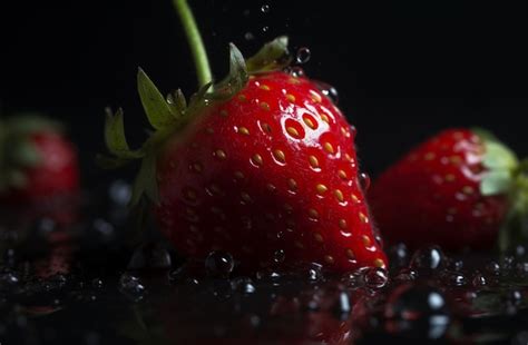 Fresas Frescas Cayendo Al Agua Con Un Toque Sobre Un Fondo Negro Foto