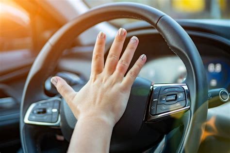 Mão feminina pressiona a buzina no volante de um carro moderno sem