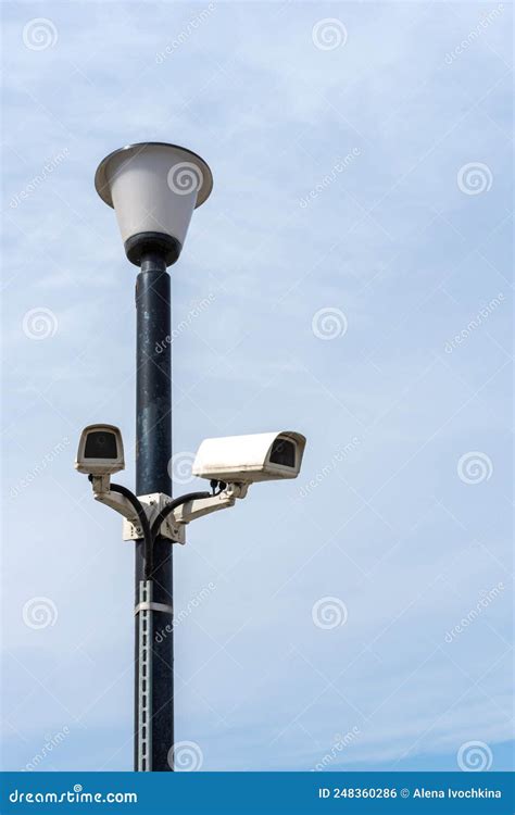 Surveillance Cameras Mounted On A Lamp Post Against A Blue Sky