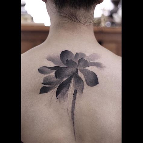 The Back Of A Woman S Shoulder With A Black And White Flower Tattoo On It