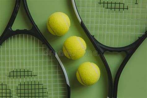 Three Tennis Balls And Two Tennis Rackets On Green Background Stock