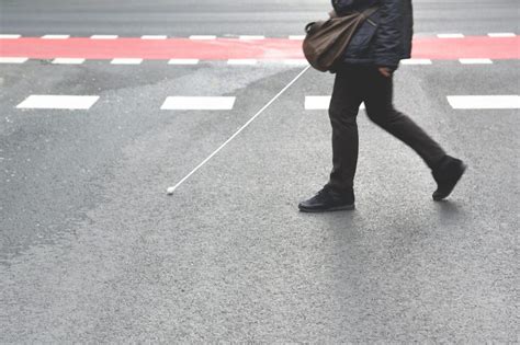 Blind person walking with a stick crossing a pedestrian walkway. Empty ...