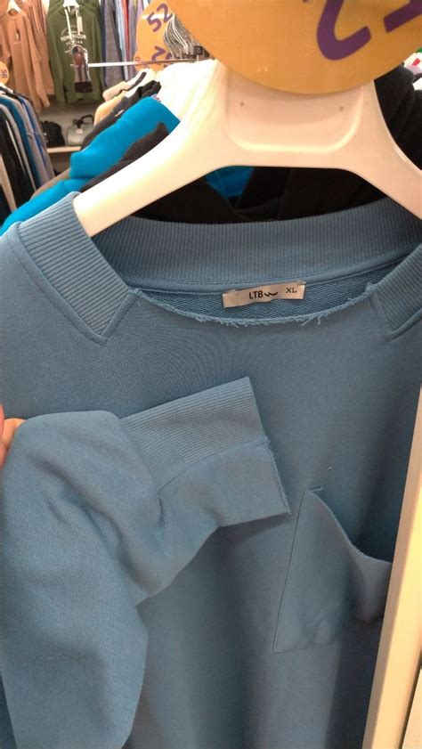 A Person Holding Onto A Blue Shirt In Front Of A Rack With Shirts On It