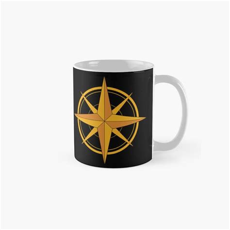 A Black And Gold Compass Mug With An Orange Star On The Center In