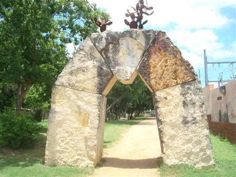 An Arch Made Out Of Rocks In The Middle Of A Grassy Area With Trees On