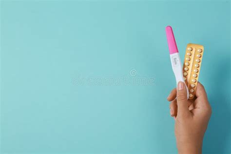 Woman Holding Birth Control Pills And Pregnancy Test On Light Blue Top