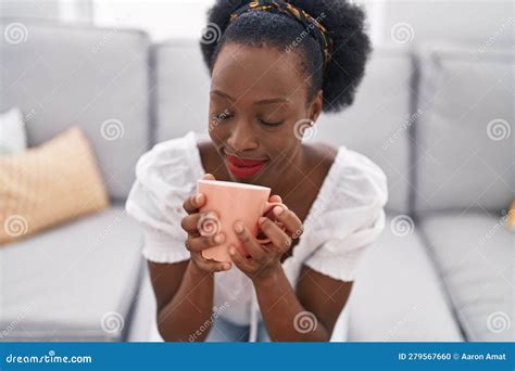 African American Woman Drinking Coffee Sitting On Sofa At Home Stock