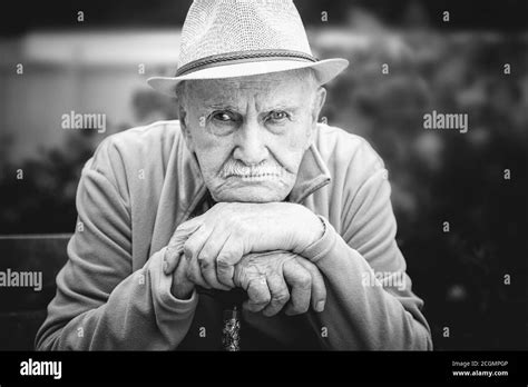 sad, angry old man in a hat is sitting in an open-air garden. the ...