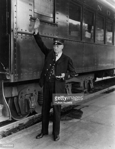 Railroad conductor standing next to a train on a track signals by ...