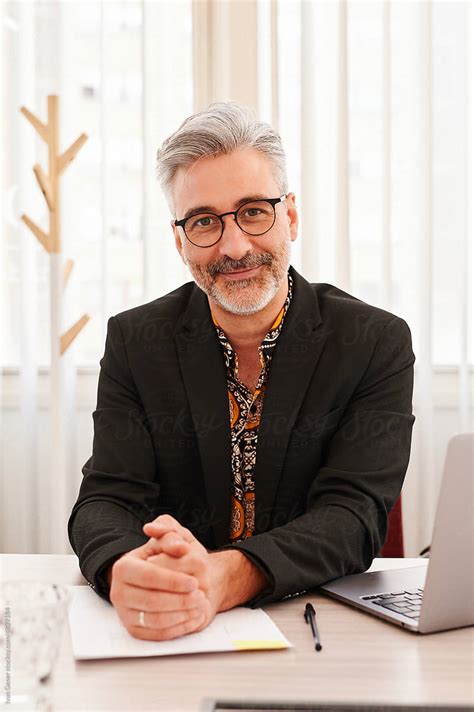 Smiling Mature Businessman Sitting At A Desk By Stocksy Contributor