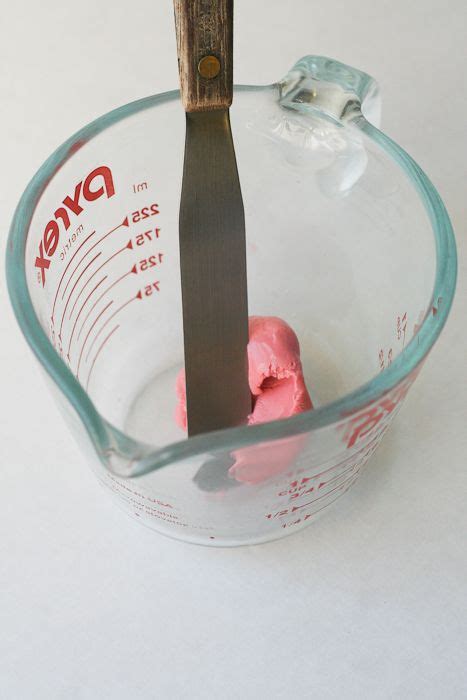 a glass measuring cup filled with pink icing and a wooden spoon sticking out of it