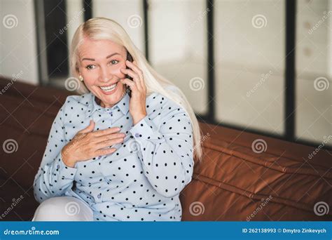 Blonde Mature Woman Talking On The Phone While Sitting On The Sofa