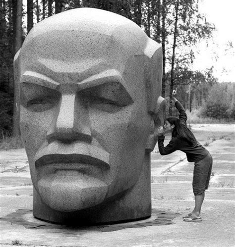 A Woman Standing In Front Of A Statue Of A Man S Head With One Hand On