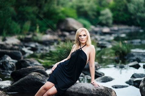 A Blonde Girl In A Black Dress With Blue Eyes On The Riverbanks Rocky